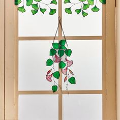 a window decorated with green and pink leaves, hanging from a wooden frame in front of a white wall