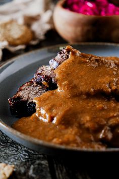 a plate with meat and gravy on it next to crackers, red cabbage