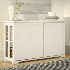 a white cabinet sitting on top of a wooden floor next to a vase and plates