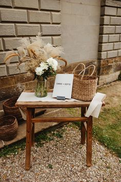 Wooden table and with flowers in glass vase and wicker basket with sign reading 'Cards Gifts' Card And Gifts Table, Picnic Basket Wedding Card Holder, Wicker Centerpiece Wedding, Gift Table Flowers Wedding, Boho Wedding Signing Table, Cards Gifts Table Wedding, Basket Card Box Wedding, Dried Flowers Wedding Decorations, Wooden Table Signs For Wedding