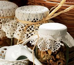 three jars with lace doily on them are sitting next to some cookies in a wicker basket