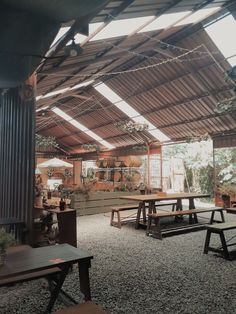 the inside of a building with tables and benches on gravel flooring, surrounded by plants