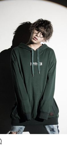 a young man wearing a green hoodie with the words emi on it, standing in front of a white wall