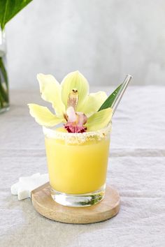 a small glass filled with yellow liquid and a flower on the top is sitting on a table