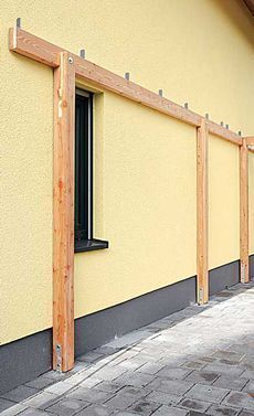 the side of a yellow building with a black window and bars on it's sides