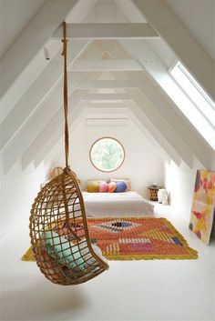 a bed sitting under a window in a bedroom next to a hanging chair and rug