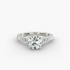 a white gold engagement ring with diamonds on the band and a round brilliant cut center stone