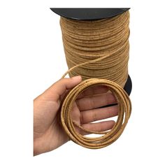 a hand holding a spool of twine in front of a roll of rope