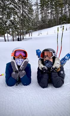 two young children sitting in the snow with skis and goggles on their faces