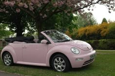 a pink convertible car parked in front of a tree