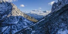 the mountains are covered in snow under a blue sky with clouds and fluffy white clouds