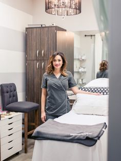 a woman standing next to a bed in a room with white furniture and striped walls