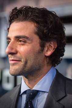 a close up of a person wearing a suit and tie with curly hair smiling at the camera