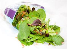 a bag of salad with lettuce and carrots on it sitting next to a pile of greens