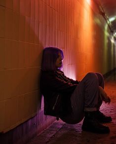 a woman sitting on the side of a building next to a wall with neon lights