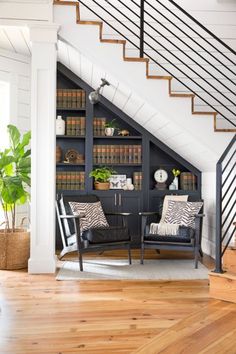 a living room with two chairs and a book shelf under the stairs in front of it