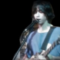 a blurry image of a person playing guitar in front of a microphone and singing into a mic