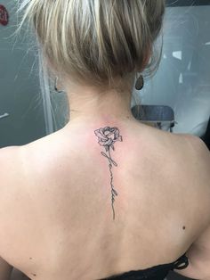 the back of a woman's neck with a single rose tattoo on her left shoulder