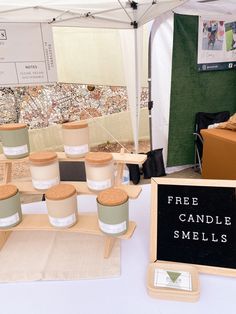 there are many candles that are on the table and in front of it is a sign with free candle smells