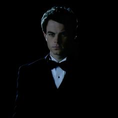 a man in a tuxedo and bow tie looking at the camera with dark background