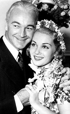 an old photo of a man and woman posing for the camera with flowers in their hair