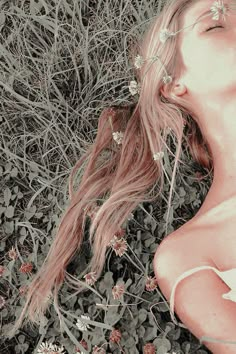 a woman laying down in the grass with her eyes closed and flowers around her head