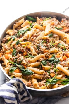 pasta with sausage and spinach in a skillet on a marble countertop next to a striped dish towel