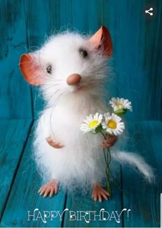 a small white rat sitting on top of a wooden table with daisies in it's paws