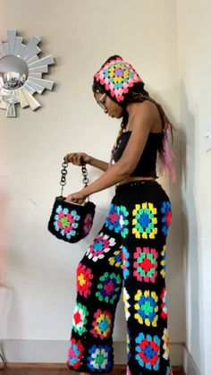 a woman is wearing colorful crocheted pants and holding a purse in her hand