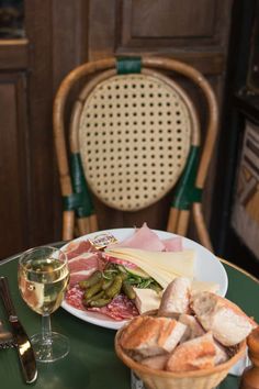 a plate with meat, cheese and bread next to a glass of wine