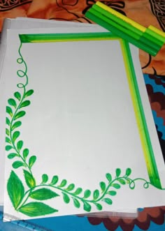 a white paper with green leaves on it next to two colored pencils and a drawing pad