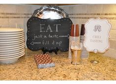 a kitchen counter topped with plates and cups next to a chalkboard that says eat just a taste fill it up