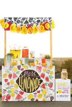 a lemonade stand on the side of a road with an umbrella and fruit sign