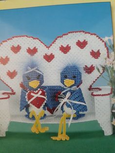 two knitted birds sitting on a bench in front of a heart - shaped frame