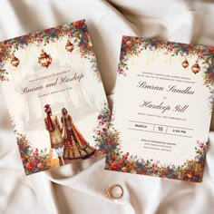 two wedding cards on top of a white sheet with colorful flowers and lanterns in the background