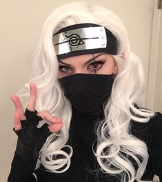 a woman with long white hair wearing a black mask and holding two fingers up in front of her face