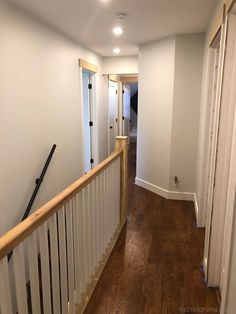 an empty hallway with wood floors and white walls, leading to a second floor bedroom