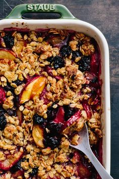 a dish filled with fruit and granola on top of a wooden table next to a spoon