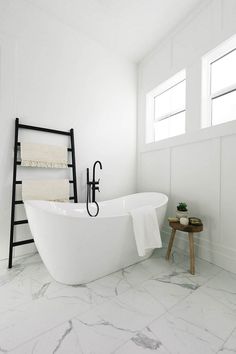 a white bath tub sitting in a bathroom next to a wooden table and ladder with towels on it