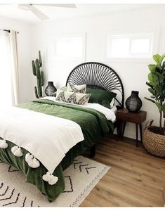 a bed with green sheets and pillows in a bedroom next to a potted plant