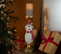 a small christmas tree with presents under it and a lit candle on the table next to it