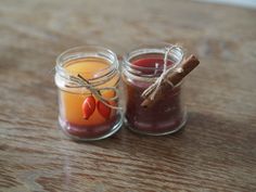 two small jars filled with different types of liquid on top of a wooden table next to a cinnamon stick