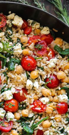 a pan filled with rice, tomatoes and spinach on top of a wooden table