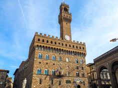 a tall brick building with a clock on it's side and people walking around