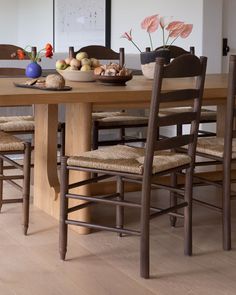 a wooden table with chairs and bowls of fruit on top of it in front of a mirror