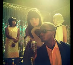 a man holding a microphone next to two women in front of a disco curtain with lights