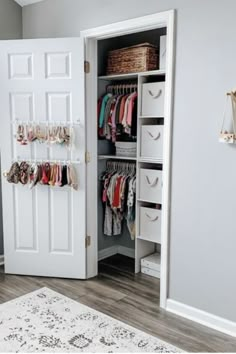 an open closet with clothes hanging on the door and baskets in front of it, next to a rug