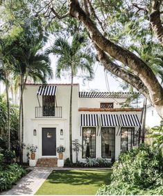 a white house with black and white striped awnings on the front door, surrounded by palm trees