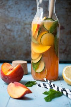 a pitcher filled with liquid next to sliced peaches and minty strawberries on a blue table