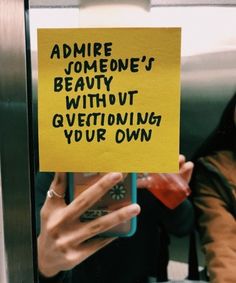 a woman holding up a yellow sign that says admire someone's beauty without questioning your own